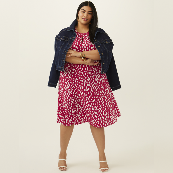 plus size woman in pink and white polka dot printed mini dress, denim jacket, and white heels