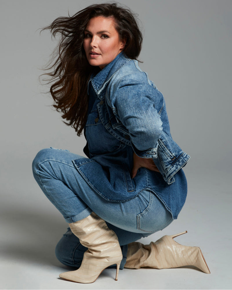 A plus-size model posing for a picture wearing a denim outfit and tan heeled boots